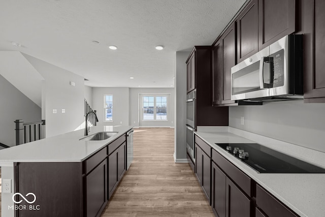 kitchen featuring dark brown cabinetry, an island with sink, light wood-style flooring, appliances with stainless steel finishes, and a sink