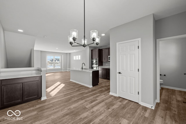 kitchen with light countertops, open floor plan, a sink, dark brown cabinets, and wood finished floors