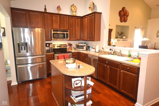 kitchen featuring appliances with stainless steel finishes, dark wood-type flooring, a peninsula, light stone countertops, and a sink