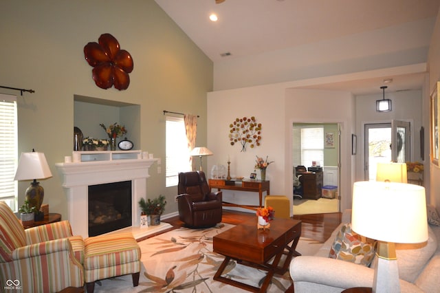 living room with recessed lighting, high vaulted ceiling, wood finished floors, and a glass covered fireplace