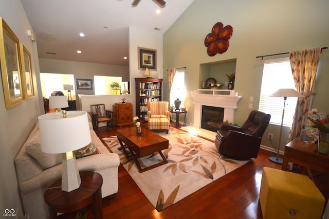 living room featuring a glass covered fireplace, recessed lighting, wood finished floors, and high vaulted ceiling