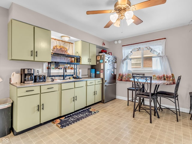 kitchen with light countertops, green cabinets, freestanding refrigerator, a sink, and baseboards