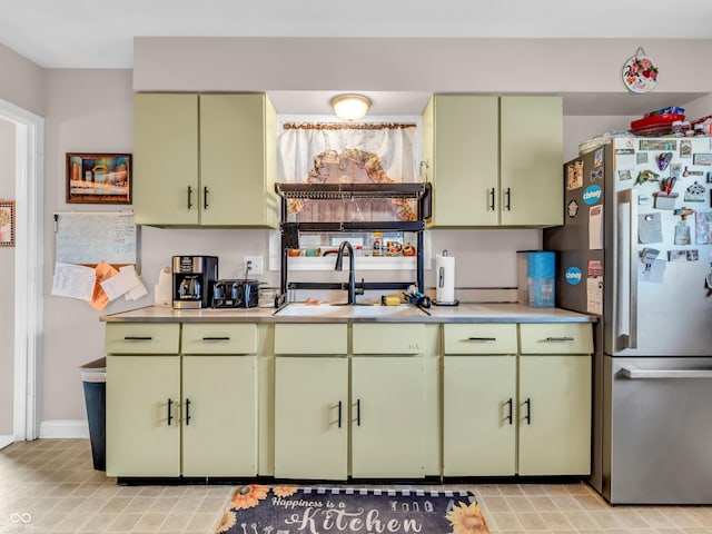 kitchen with light countertops, green cabinets, yellow cabinetry, freestanding refrigerator, and a sink