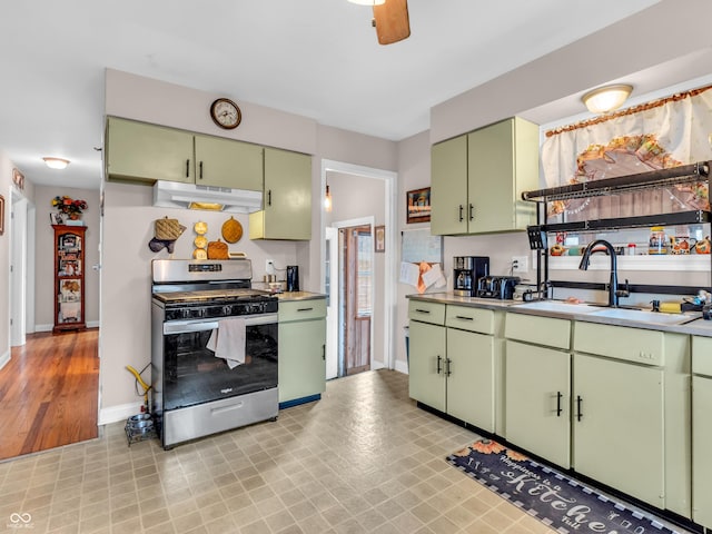 kitchen with under cabinet range hood, a sink, light countertops, stainless steel range with gas cooktop, and green cabinetry