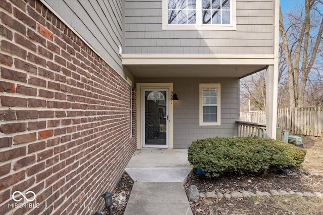 view of exterior entry featuring brick siding and fence