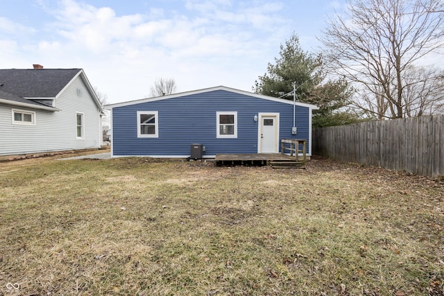 rear view of house featuring central AC unit, fence, and a lawn