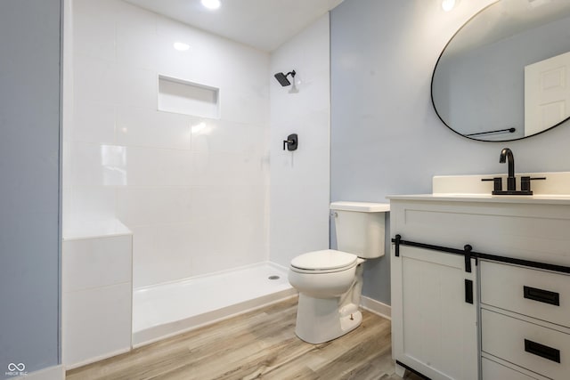 full bathroom featuring a tile shower, vanity, wood finished floors, and toilet