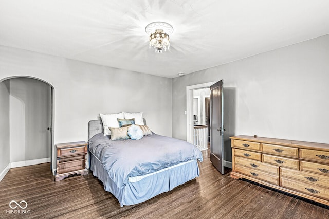 bedroom with dark wood-style floors, arched walkways, and baseboards