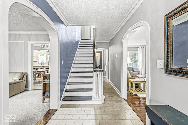 foyer featuring arched walkways, ornamental molding, a textured ceiling, and stairs