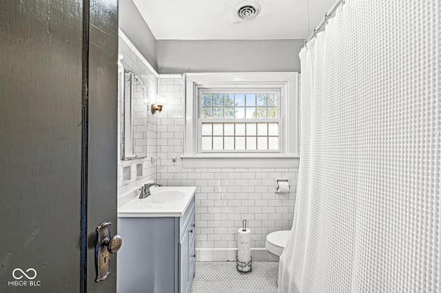 bathroom with tile walls, visible vents, toilet, vanity, and tile patterned flooring