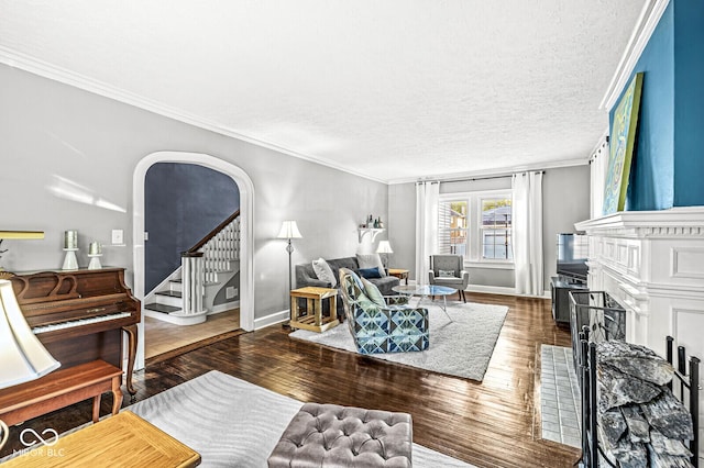 living area featuring arched walkways, a fireplace with flush hearth, wood finished floors, stairs, and crown molding