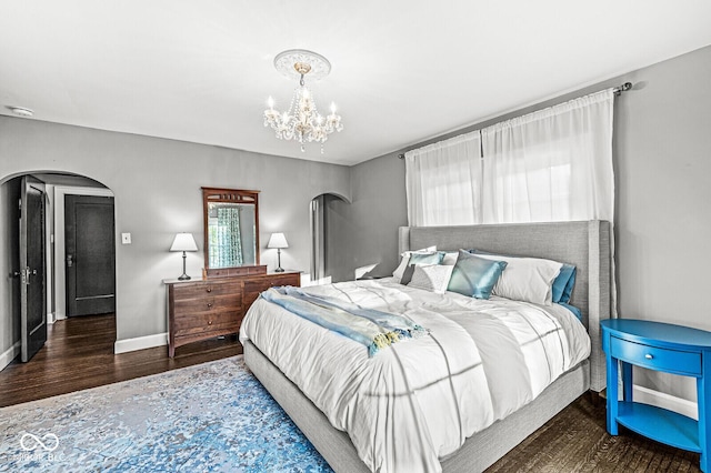 bedroom featuring arched walkways, baseboards, wood finished floors, and a notable chandelier