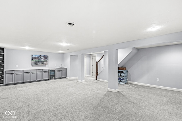 finished basement with beverage cooler, visible vents, stairs, wet bar, and carpet