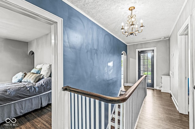 corridor with a textured ceiling, arched walkways, crown molding, and wood finished floors