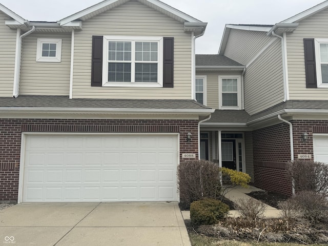 view of front of house featuring a garage, roof with shingles, concrete driveway, and brick siding