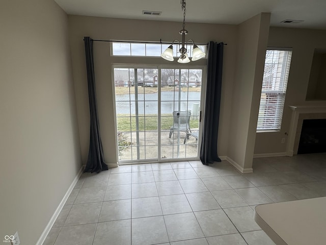 unfurnished dining area featuring a fireplace, a notable chandelier, light tile patterned floors, a water view, and baseboards