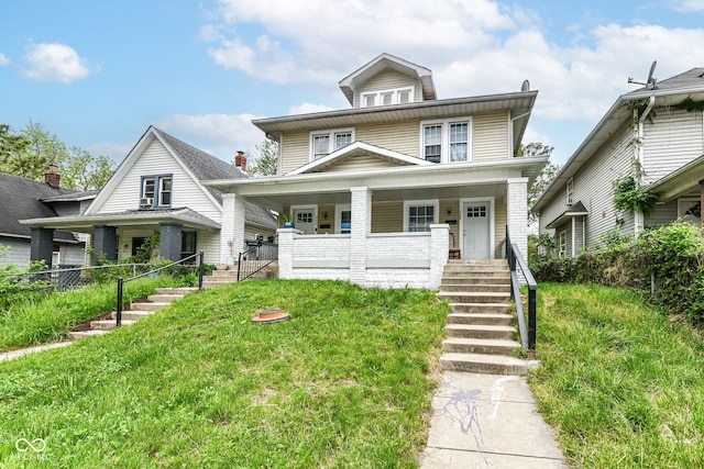 american foursquare style home featuring covered porch, stairs, and a front yard