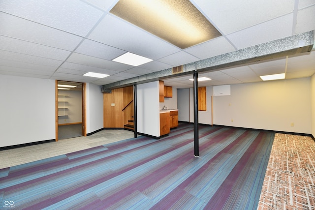 finished basement featuring a paneled ceiling, stairway, and baseboards