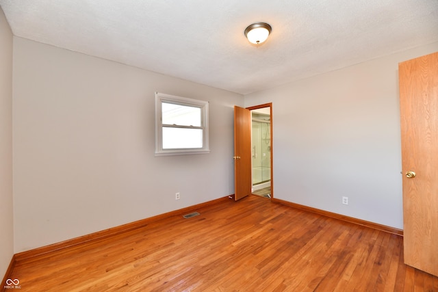 empty room with baseboards, visible vents, a textured ceiling, and light wood finished floors