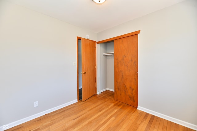 unfurnished bedroom with light wood-type flooring, baseboards, and a closet