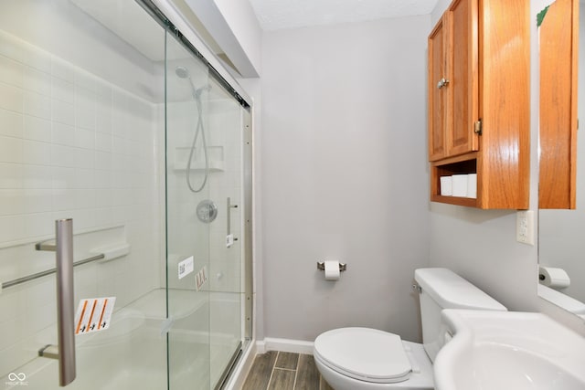 bathroom featuring toilet, a stall shower, wood tiled floor, a sink, and baseboards