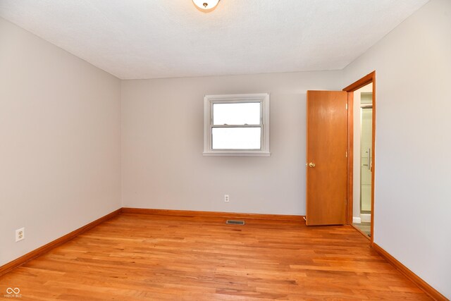 spare room with light wood-type flooring, visible vents, and baseboards