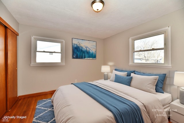 bedroom featuring a closet, multiple windows, wood finished floors, and baseboards