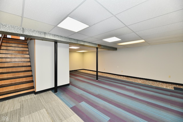 finished basement featuring a paneled ceiling, stairs, baseboards, and carpet flooring