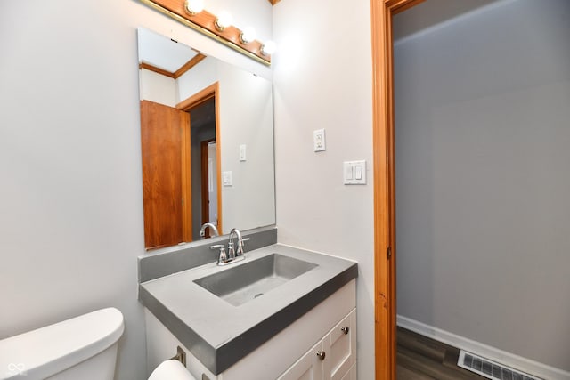 bathroom with visible vents, toilet, vanity, wood finished floors, and baseboards