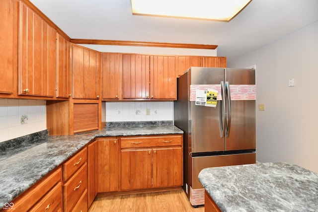 kitchen with light wood-style floors, brown cabinets, backsplash, and freestanding refrigerator