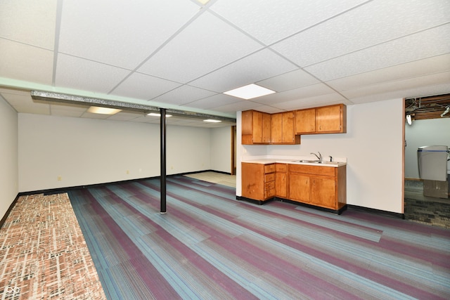 finished basement with a drop ceiling, a sink, and baseboards