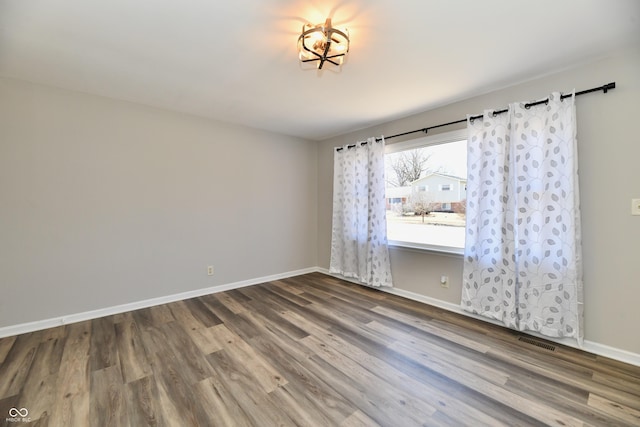 unfurnished room featuring wood finished floors, visible vents, and baseboards