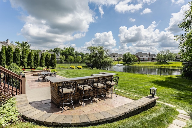 view of patio / terrace featuring a water view, a fire pit, fence, and outdoor dry bar