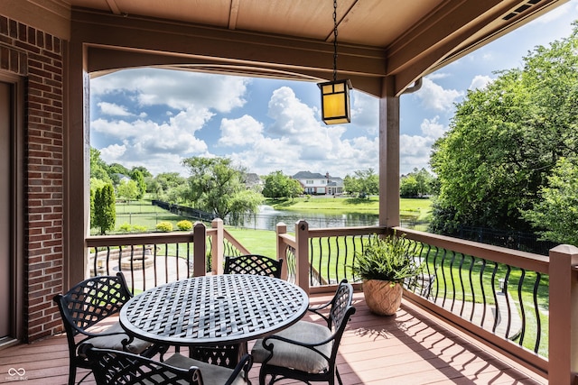 wooden terrace featuring a yard, outdoor dining area, a water view, and fence