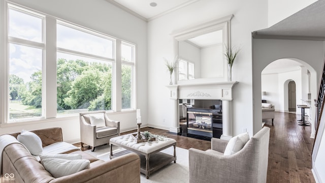 living area with arched walkways, baseboards, wood finished floors, and crown molding