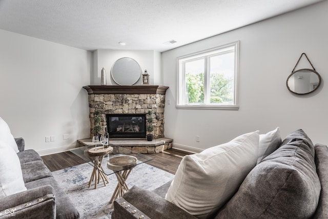 living area featuring a textured ceiling, a stone fireplace, wood finished floors, visible vents, and baseboards