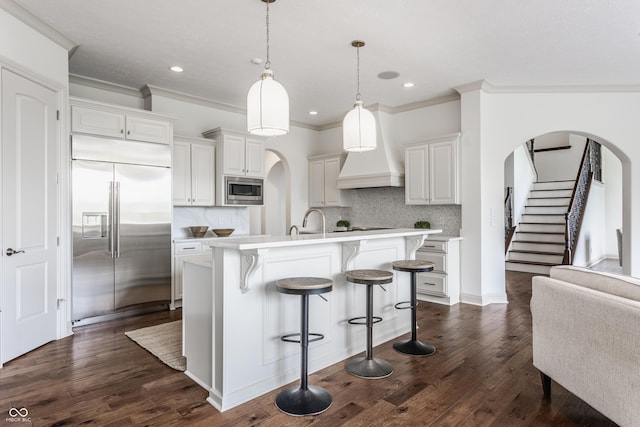 kitchen with built in appliances, light countertops, arched walkways, and dark wood-style floors