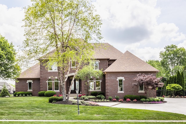 view of front of house with driveway, brick siding, a shingled roof, and a front yard