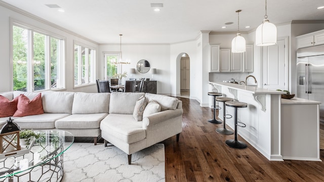 living room featuring ornamental molding, arched walkways, dark wood finished floors, and recessed lighting