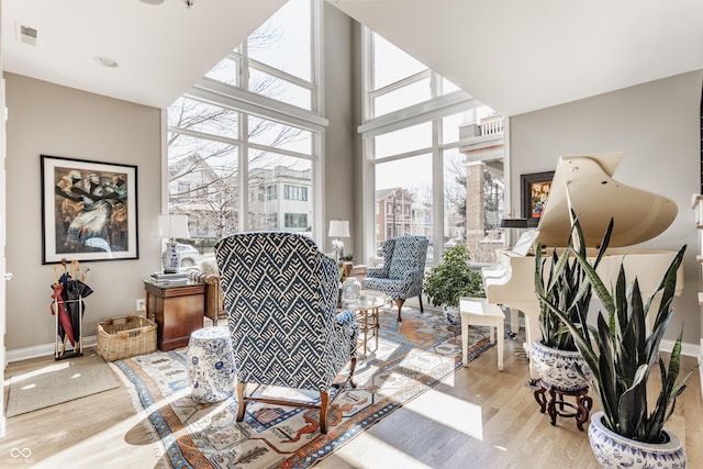 living area featuring visible vents, a towering ceiling, baseboards, and wood finished floors