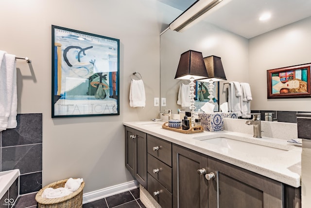 full bath with tile patterned floors, double vanity, baseboards, and a sink