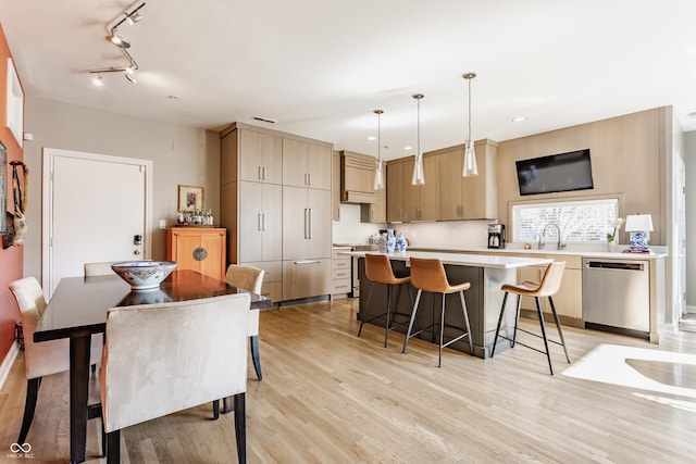 kitchen featuring light wood-type flooring, a kitchen island, stainless steel dishwasher, a breakfast bar area, and light countertops