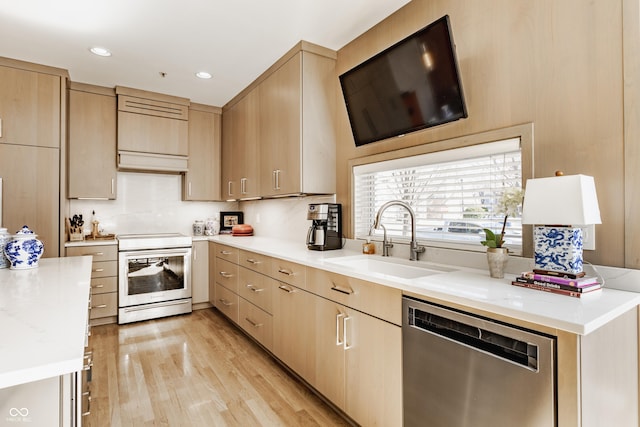 kitchen with a sink, light brown cabinetry, light countertops, stainless steel appliances, and light wood-type flooring