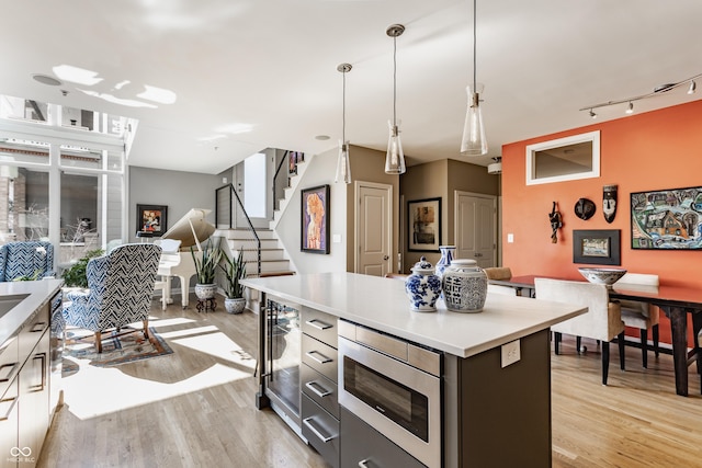 kitchen with stainless steel microwave, a center island, open floor plan, light countertops, and light wood-style floors