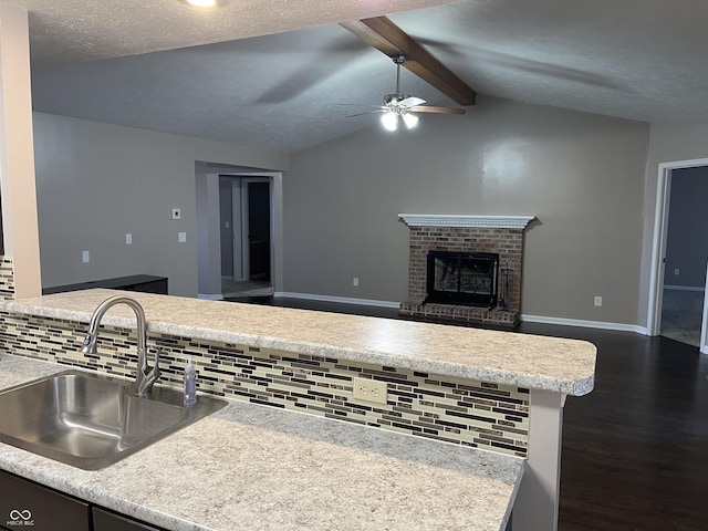 kitchen featuring dark wood finished floors, lofted ceiling with beams, a fireplace, a sink, and decorative backsplash