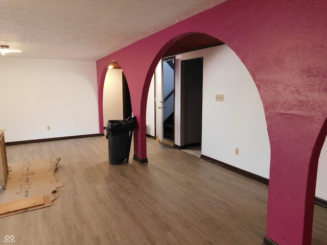 empty room with arched walkways, a textured ceiling, wood finished floors, and baseboards