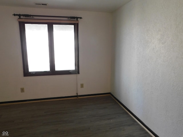 empty room with wood finished floors, visible vents, and baseboards