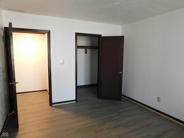 unfurnished bedroom featuring a closet, visible vents, baseboards, and wood finished floors