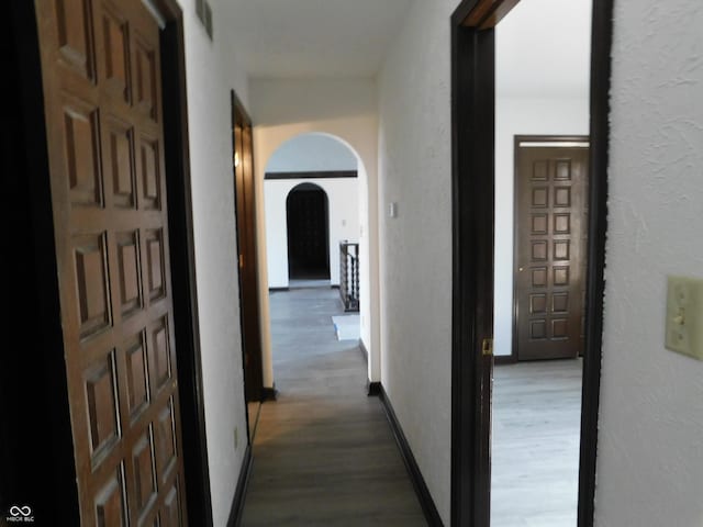 corridor with dark wood-style floors, baseboards, and arched walkways