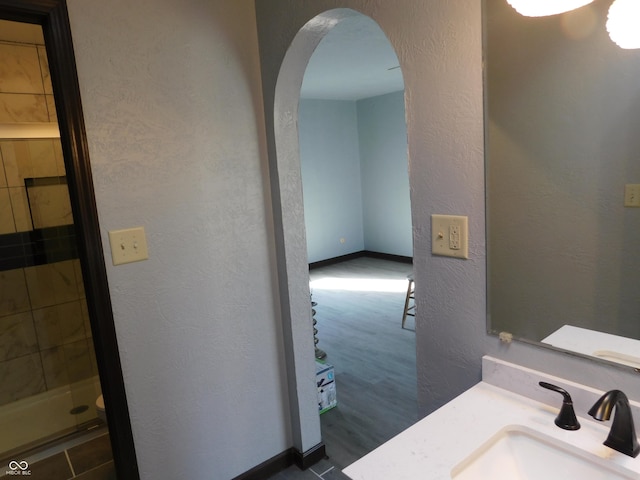 full bath with a textured wall, a shower stall, baseboards, and vanity